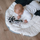 Baby lying on a white cushion with a black and white patterned blanket