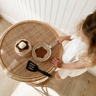 Child playing with a toy kitchen set on a round wicker table.