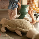 Large plush turtle toy on a floor with people in the background