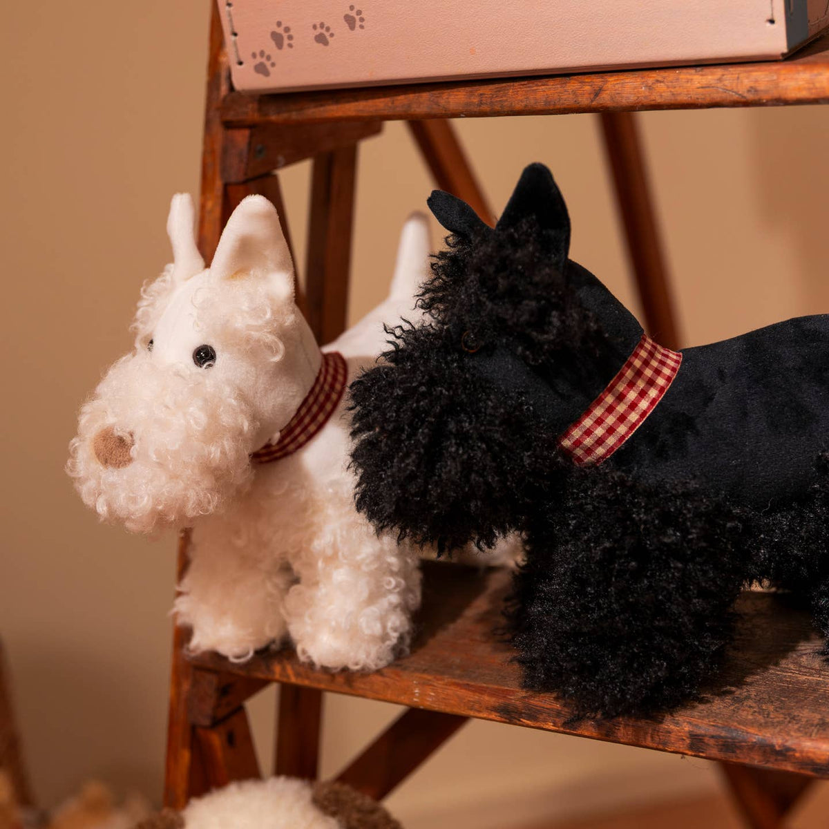 Two plush toy dogs, one white and one black, sitting on a wooden stool.