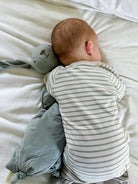 Baby in a striped onesie lying on a white bed with a soft toy.