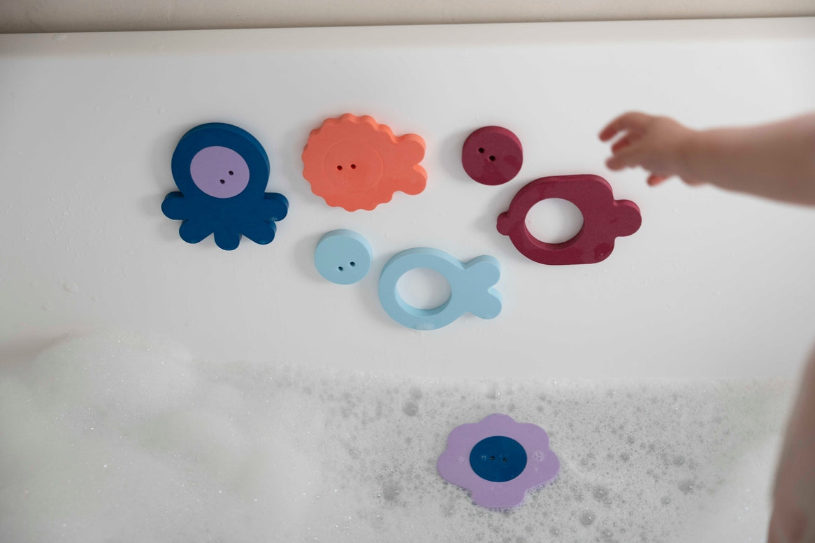 Colorful bath toys on a white surface with a child's hand reaching out.