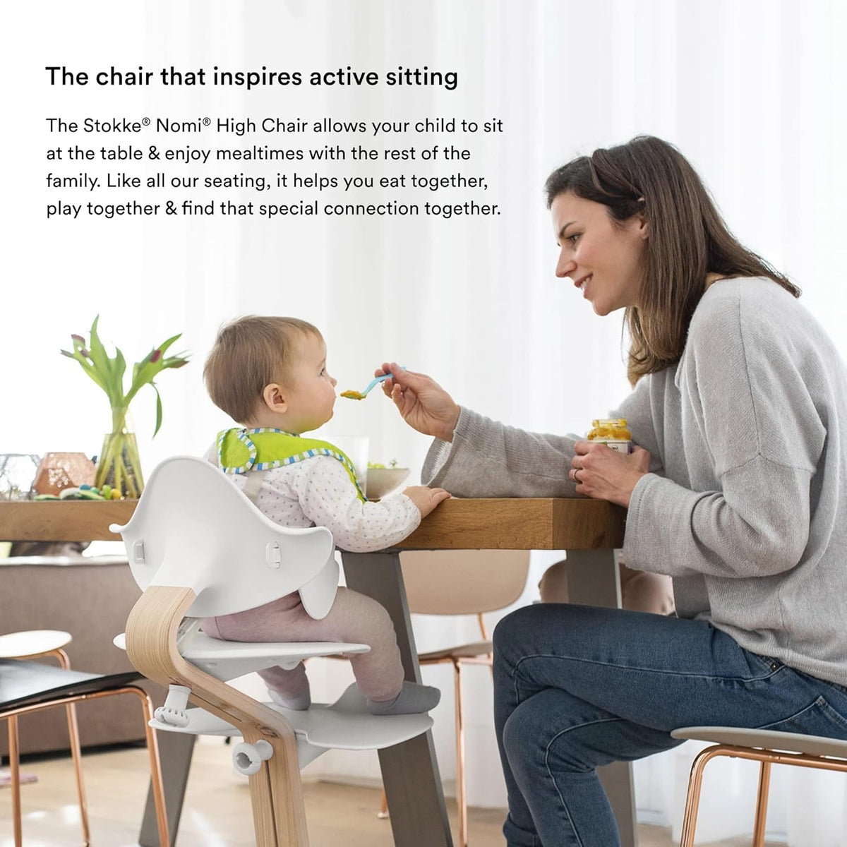 Woman feeding a child in a high chair at a dining table.