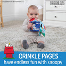 Baby holding a book with Snoopy on a carpeted floor, Peanuts branding visible.