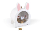 A white rabbit-shaped coin jar with pink inner ears and a cartoon face, shown on a clean white background with coins inside and one coin in front.