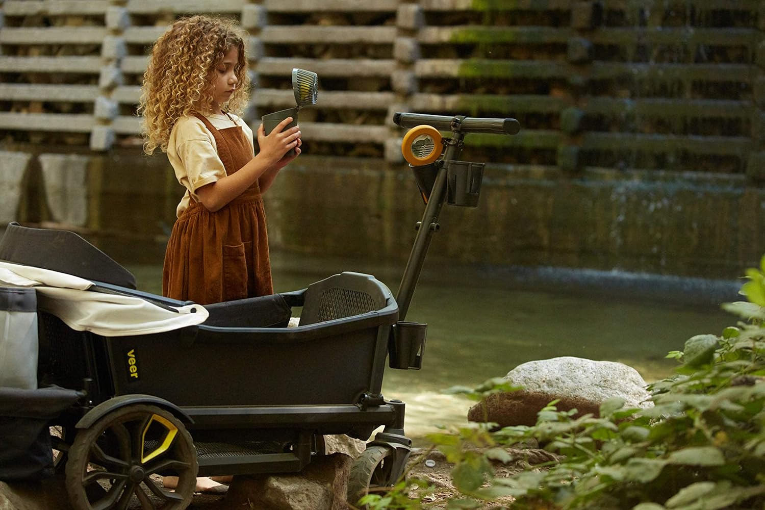 Child playing with a toy shovel and wheelbarrow by a pond