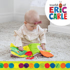 Baby playing with a colorful book, sitting on a carpeted floor with 'World of Eric Carle' logo.