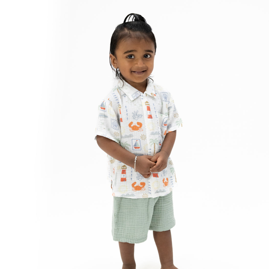 Young girl wearing a patterned shirt and green shorts on a white background