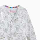 A close-up of a baby long-sleeve sleep suit or pajama top with an all-over print of gray crescent moons, owls, and small gold stars on a white background. The inside collar shows the 'eco-friendly magnetic me' brand label.