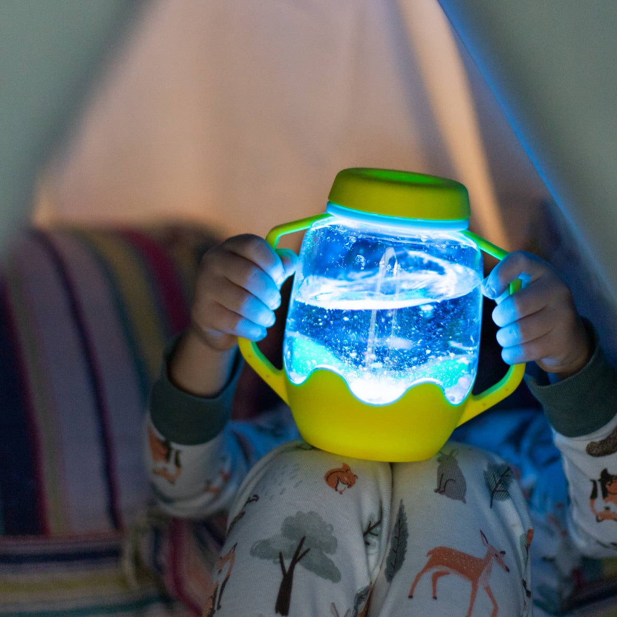 Child holding a glowing jar with a blue light inside, sitting in front of a lamp.