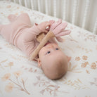 Baby lying on a floral crib sheet with a toy, looking up.