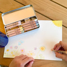 Person coloring a drawing of flowers with colored pencils on a wooden table.