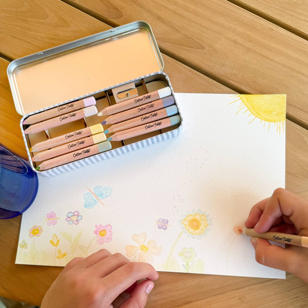 Person coloring a drawing of flowers with colored pencils on a wooden table.