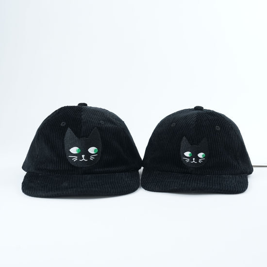 Two black caps with cat face designs on a white background