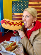 Person holding a hot dog-shaped bag with a sandwich on a table in front of an American flag.