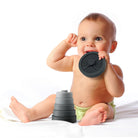 Baby playing with a black teething ring and gray stacking toys on a white background