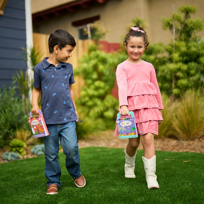 Two children standing outdoors holding colorful packages, with a house and garden in the background.
