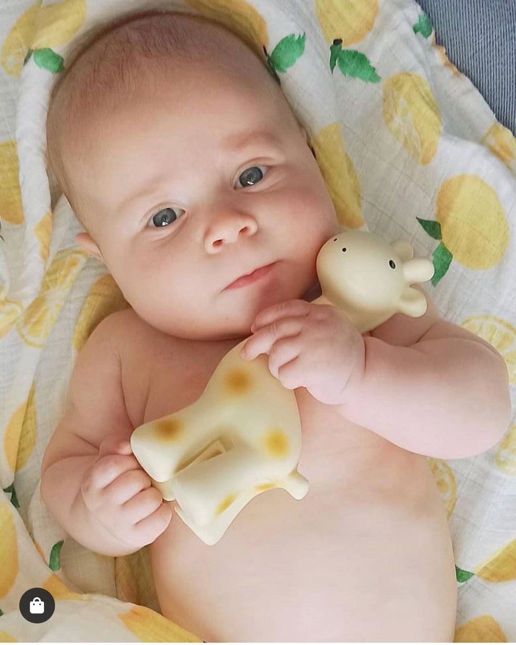 Baby holding a teething toy on a lemon-patterned blanket