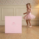Pink baby album with a child in a pink dress standing in the background