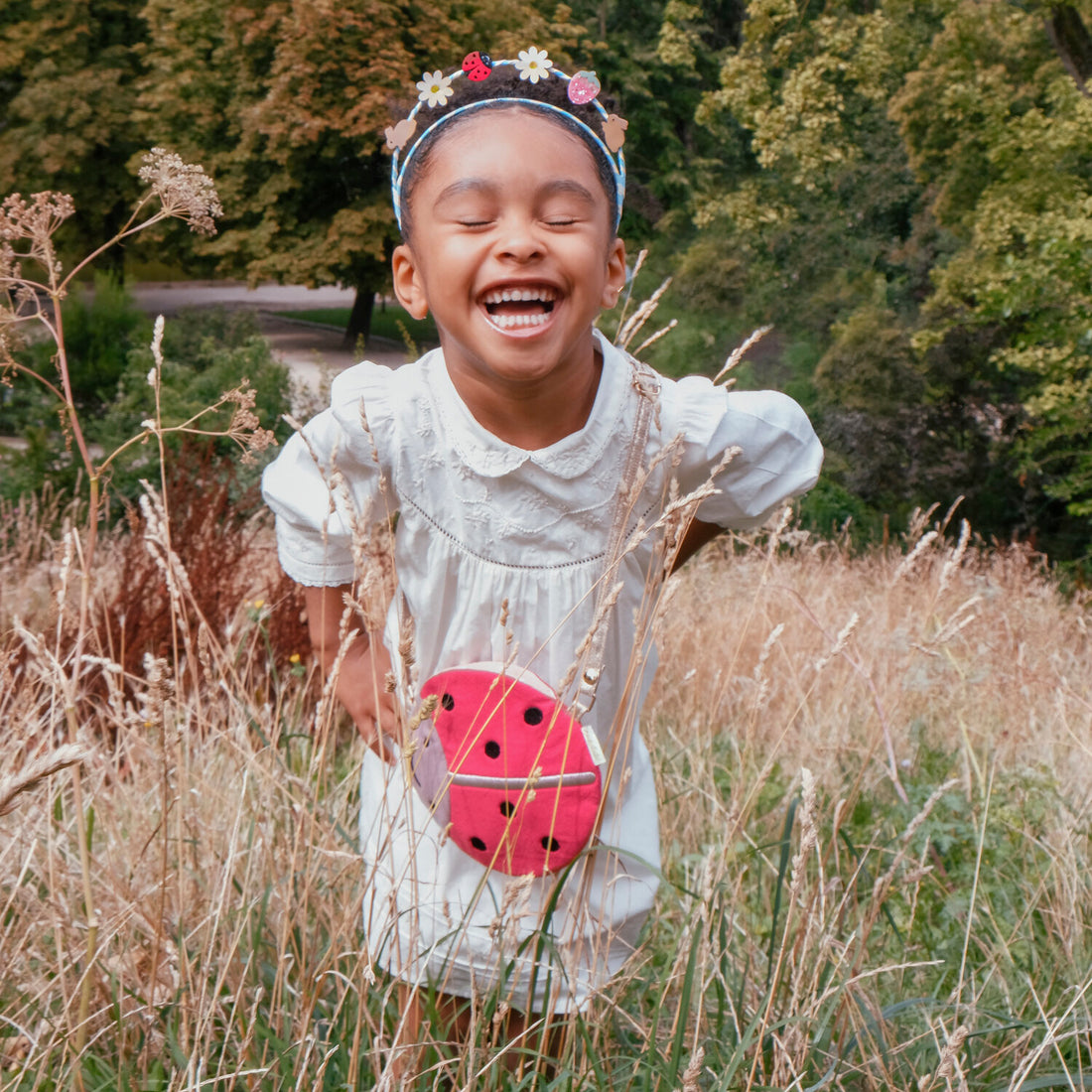 Child in a white dress with a ladybug toy standing in tall grass