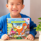 Child holding a dinosaur coloring book with a plant in the background