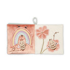 A square soft fabric book or pouch with a hanging loop, featuring embroidered bee and flower designs on a split pink and cream background.
