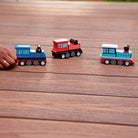 Three toy trains on a wooden surface with a hand interacting with one of them.