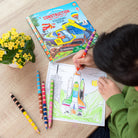 Child coloring a rocket ship with a construction-themed coloring book and crayons on a wooden table.
