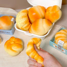 Baked goods in a white container with a hand holding a bread roll on a light surface.