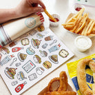 Coloring book with food illustrations next to snacks on a table.