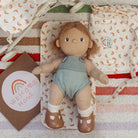 Toy baby in a green outfit with a rainbow card on a patterned blanket