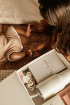 Child holding hands with an adult next to a box of L'OCCITANE products on a wooden floor.