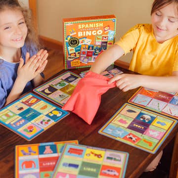Two children playing with a Spanish bingo game on a wooden table.