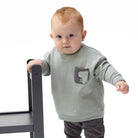 A baby wearing a light gray long-sleeve crewneck sweatshirt with a small dark gray graphic on the left chest, displayed flat against a solid white background.