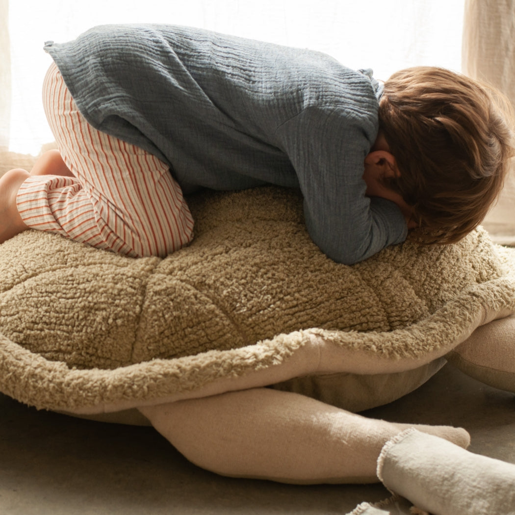 Child playing on a large plush turtle toy in a cozy room.