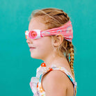 Young girl wearing pink swim goggles and a colorful swimsuit against a teal background