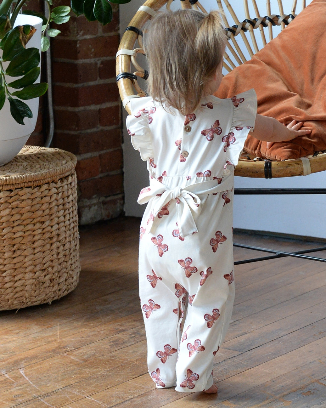 Child wearing a white romper with pink floral patterns in a home setting.