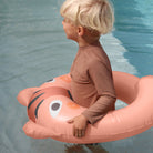 Child sitting on a tiger-shaped inflatable pool float in a pool