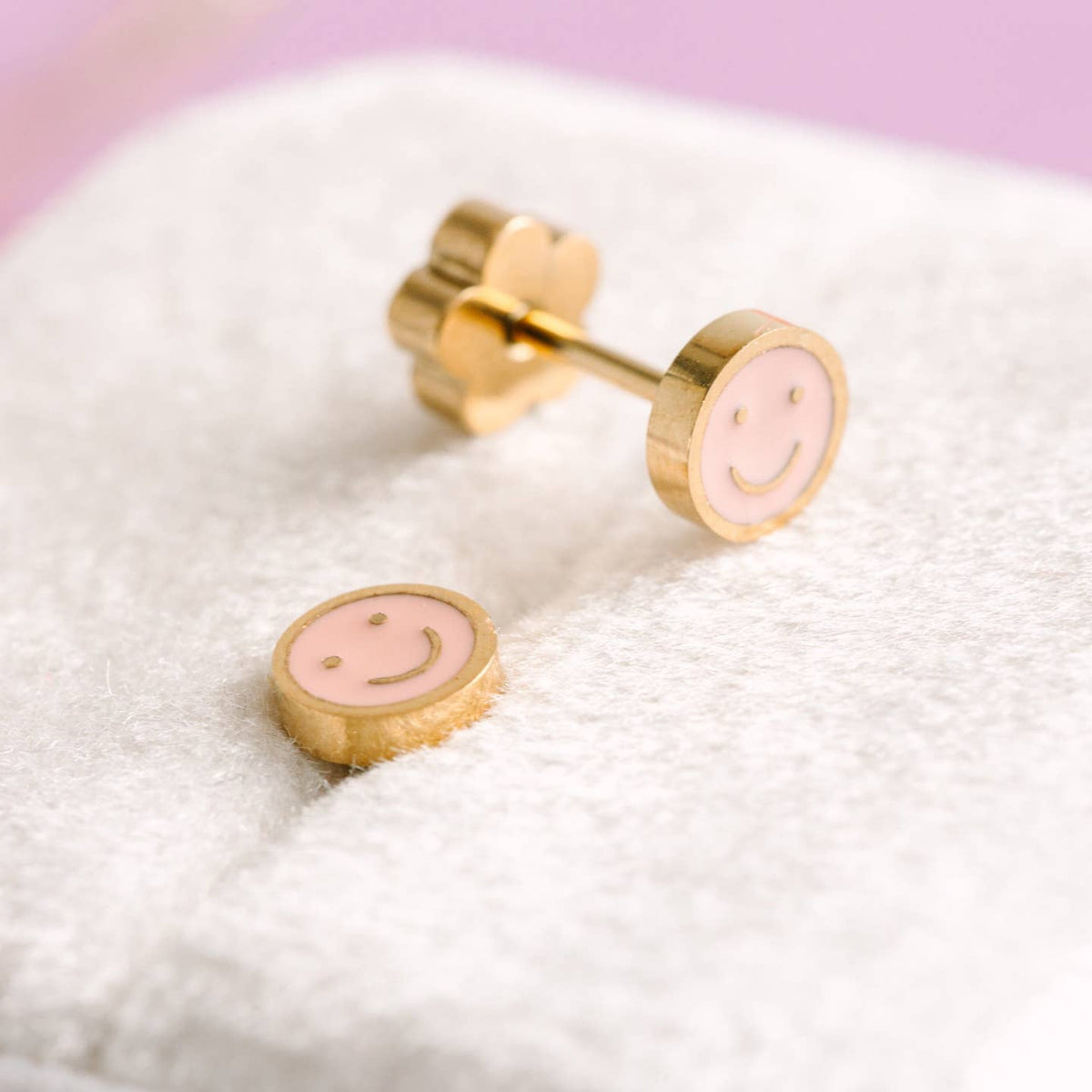 Pink smiley face earrings with gold accents on a white surface.
