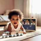 Child playing with wooden toy train set on a light-colored floor.