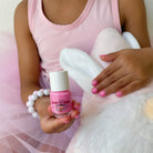 Child in pink dress holding a bottle of pink nail polish with a white cap.