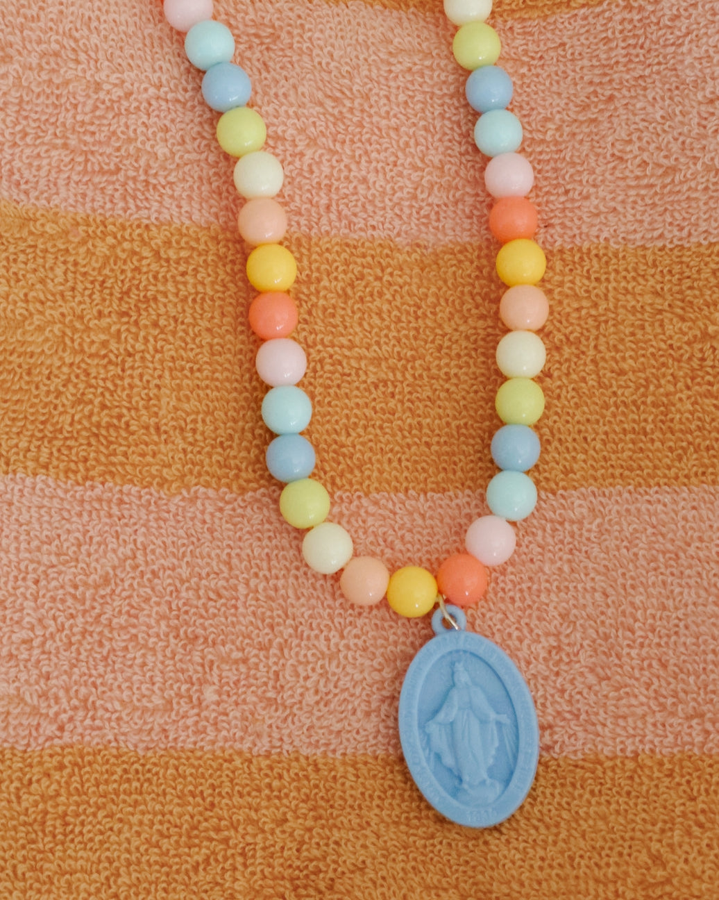 Necklace with pastel beads and a blue pendant on an orange and brown striped fabric background