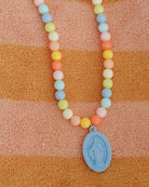 Necklace with pastel beads and a blue pendant on an orange and brown striped fabric background