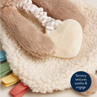 Heart-shaped toy with textured handle on a soft surface, featuring colorful ribbons.