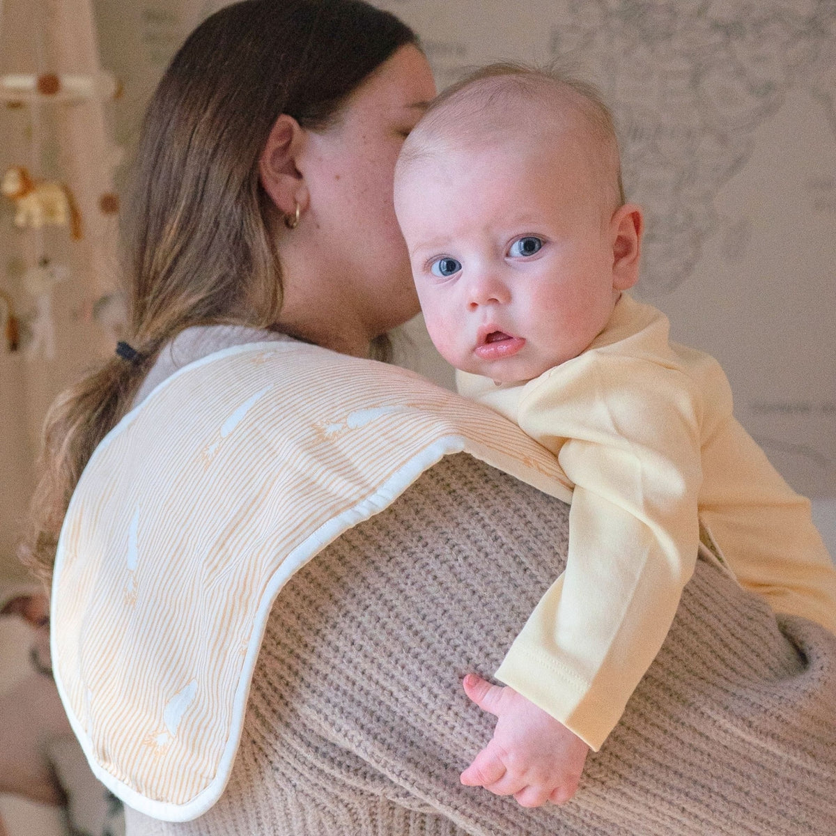Woman holding a baby in a yellow outfit in a nursery setting