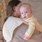 Woman holding a baby in a yellow outfit in a nursery setting