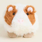 A plush guinea pig toy with fluffy white and brown fur, pink inner ears and nose, and small black eyes, photographed on a plain light beige background.