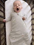 Baby in a swaddle with duck pattern yawning in a crib