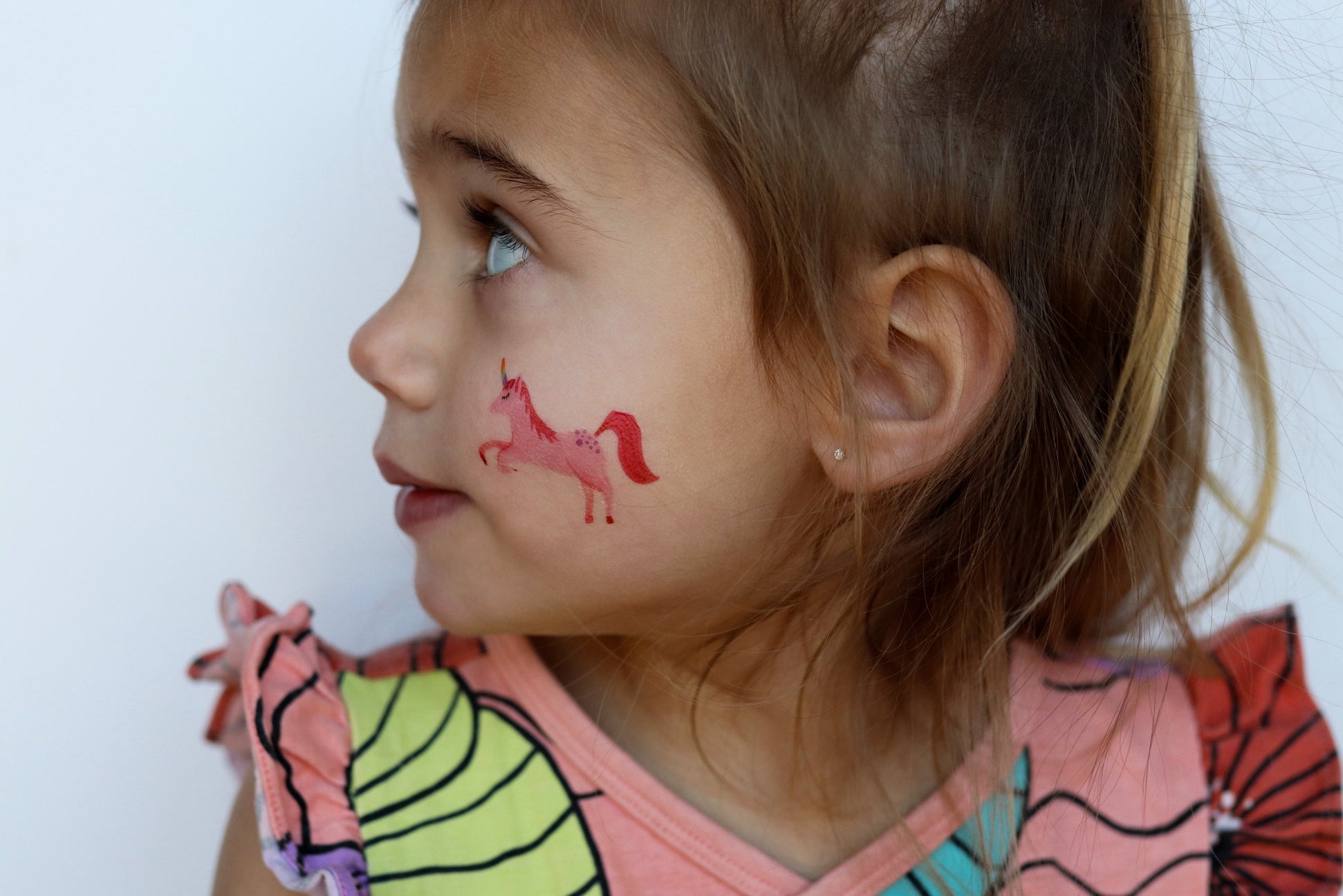 Young girl with a red unicorn face paint on her cheek against a white background