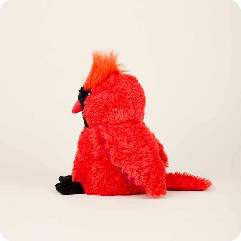 A side-profile view of the Red Cardinal by Warmies plush toy, showcasing its bright red fuzzy fur, textured crest, black face with a red beak, and soft black feet against a neutral background.